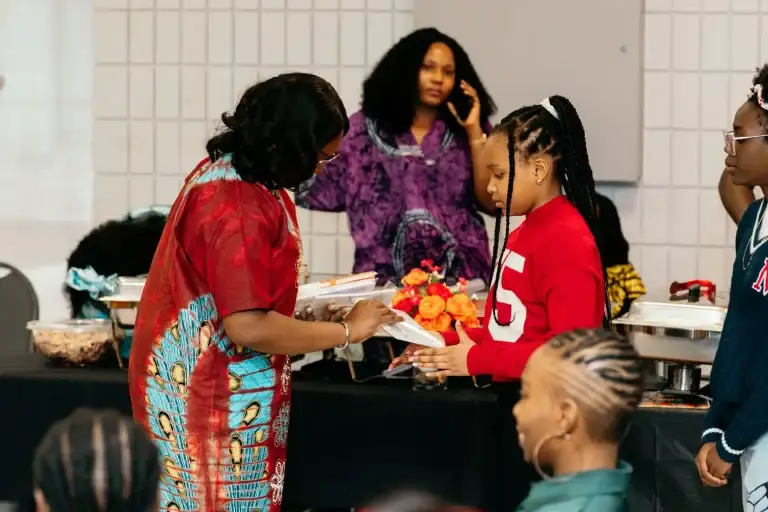 A young attendee receiving an event programme from an organiser in traditional dress
